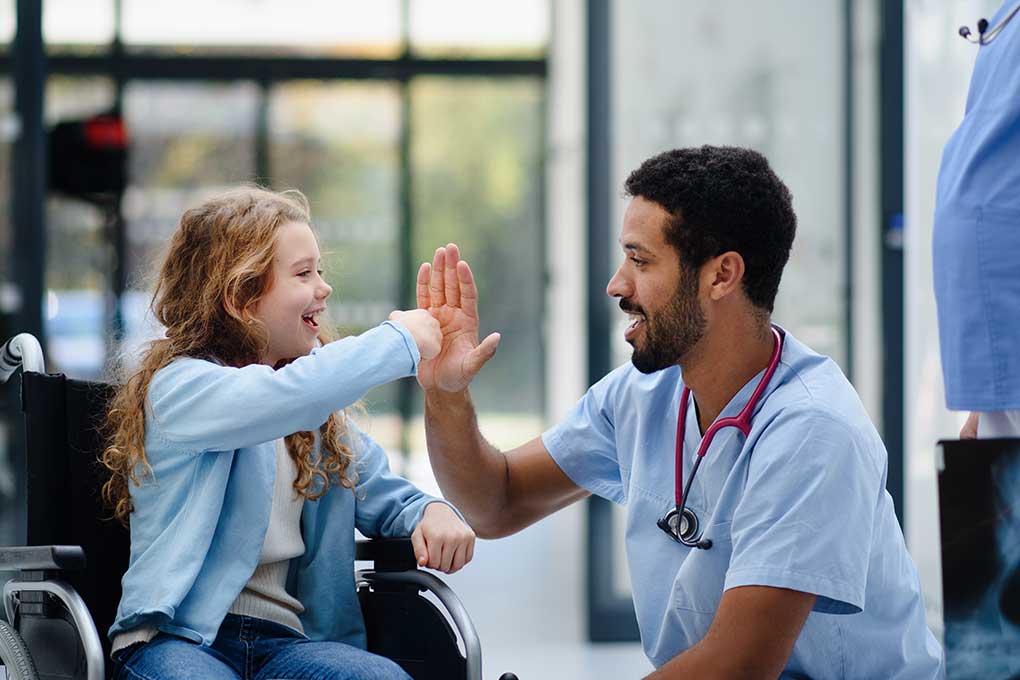 Young doctor high-fiving little girl in a wheelchair